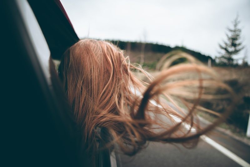 Chica peliroja que está de espaldas en la ventanilla del coche con el pelo que vuela por el viento